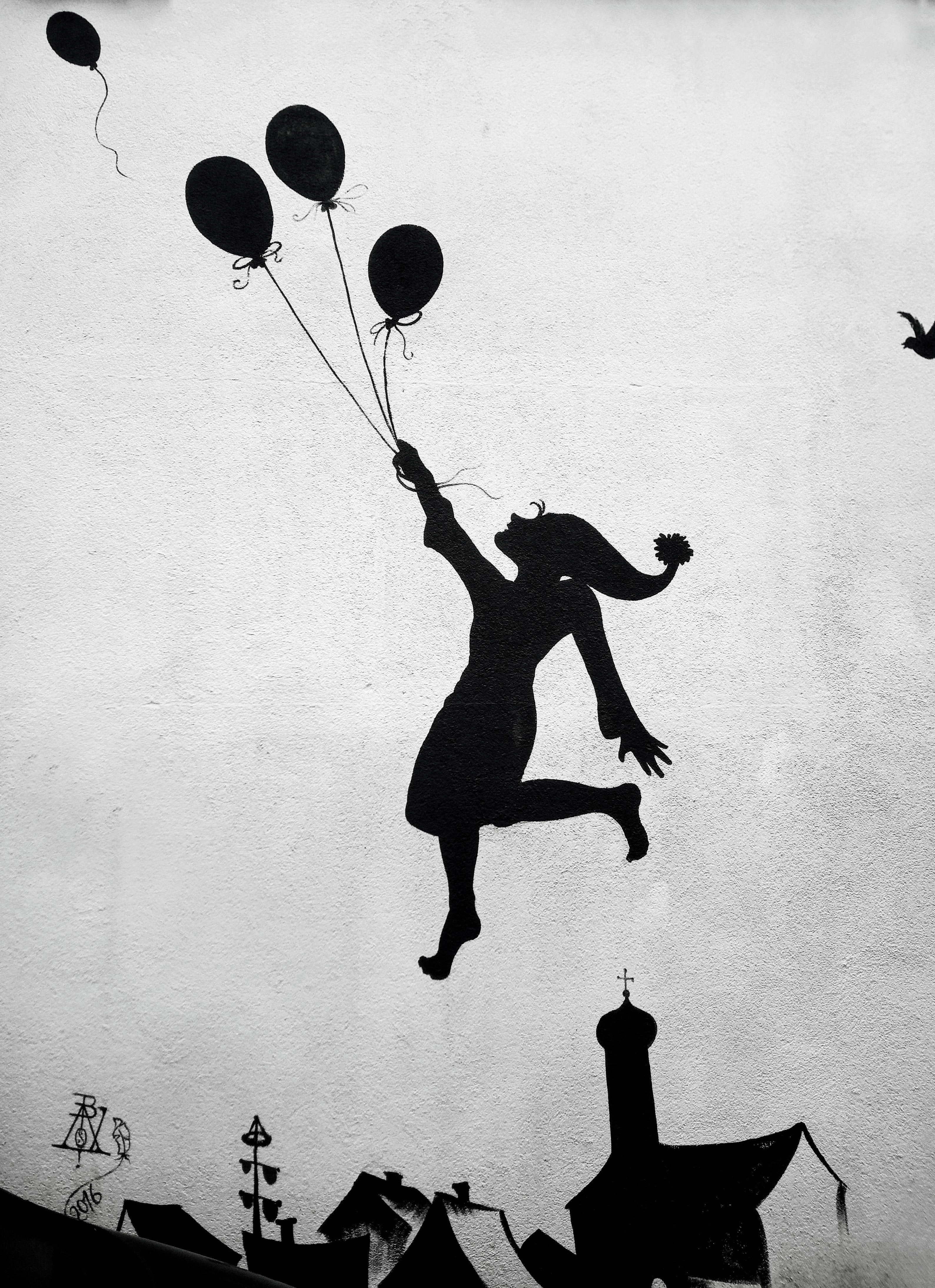 A silhouette of a girl holding balloons above rooftops