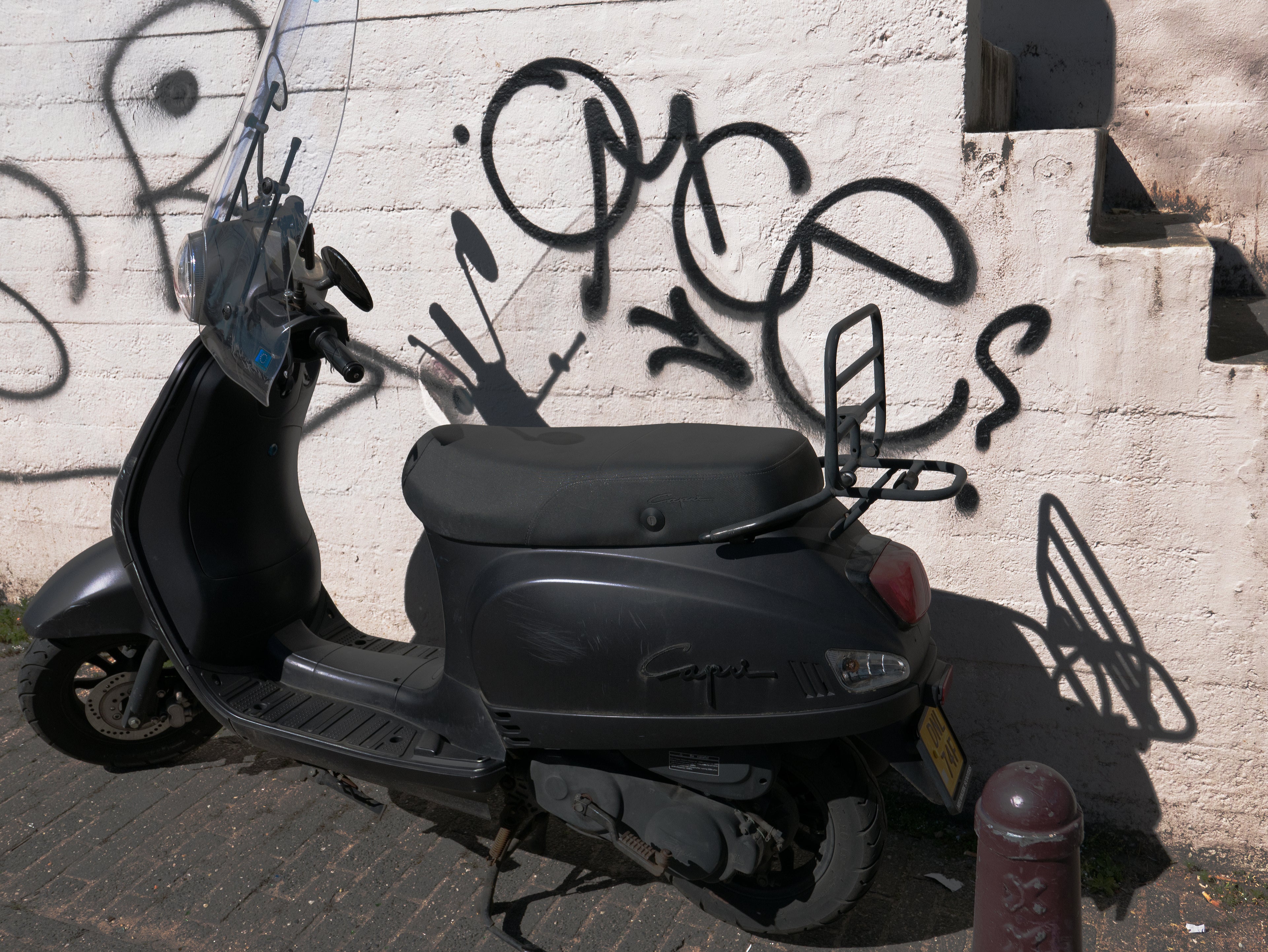 A gray moped parked in front of a white wall covered in spray-painted graffiti tags, Amsterdam