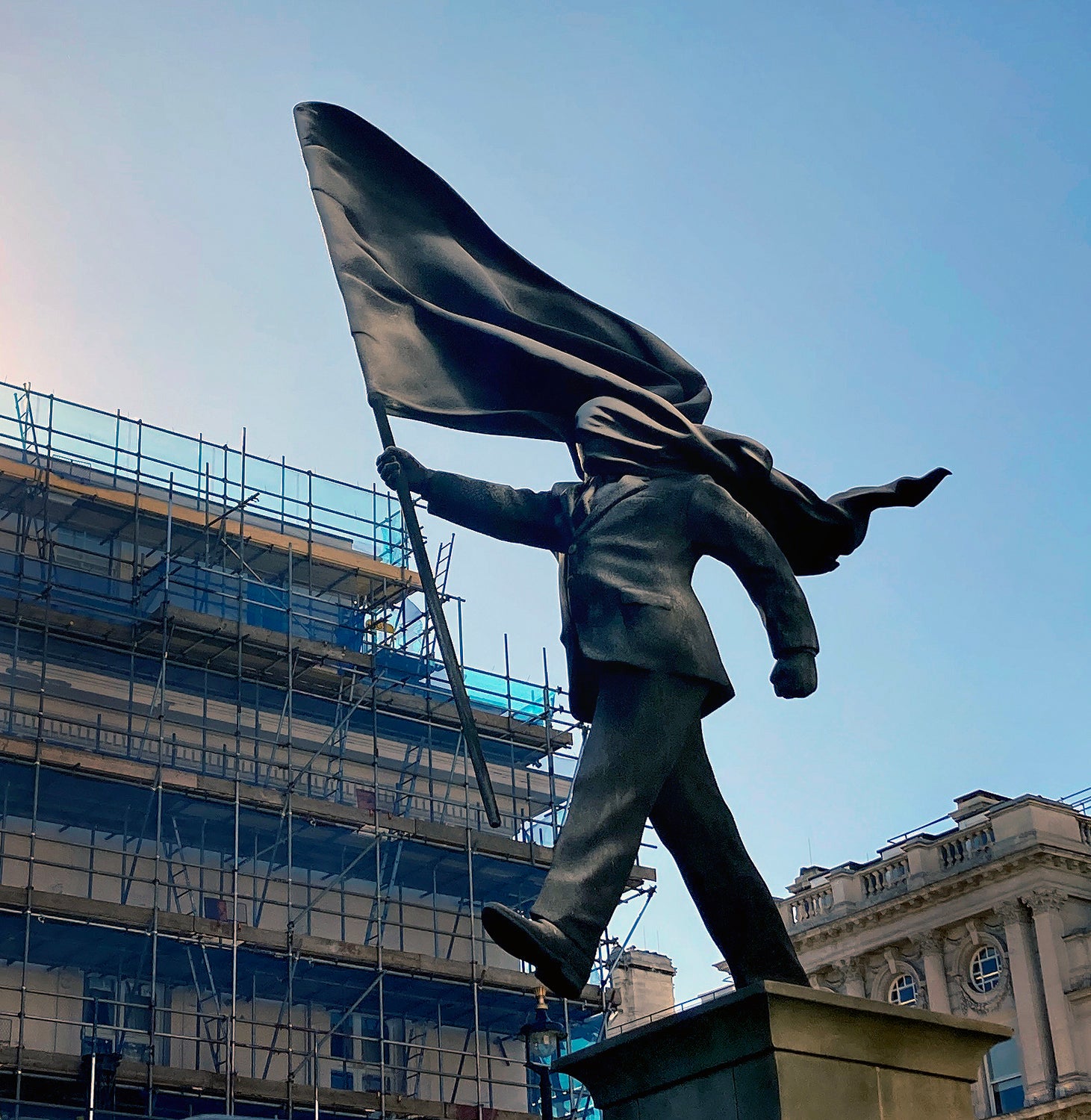 Banksy's Flag Man statue in Waterloo Place, London, a suited figure blinded by a wind-blown flag as he steps off a plinth