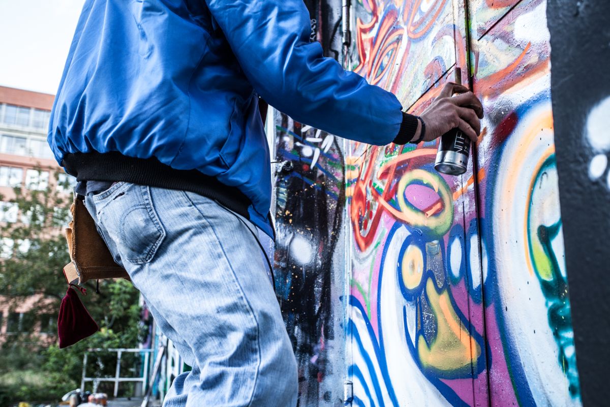 Person physically painting a large graffiti mural on a wall by hand contrasting human art with AI generation